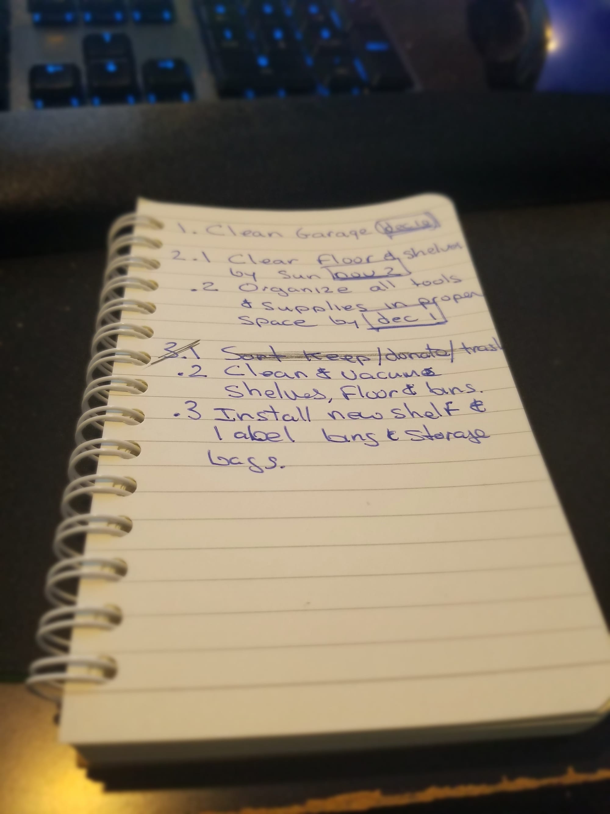 Photo of a handwritten 1-2-3 Focus Plan in a spiral notebook titled ‘Clean Garage.’ The plan lists one goal to clean the garage, two milestones — clearing the floor and organizing tools — and three weekly actions including sorting items, cleaning shelves, and installing new storage.
