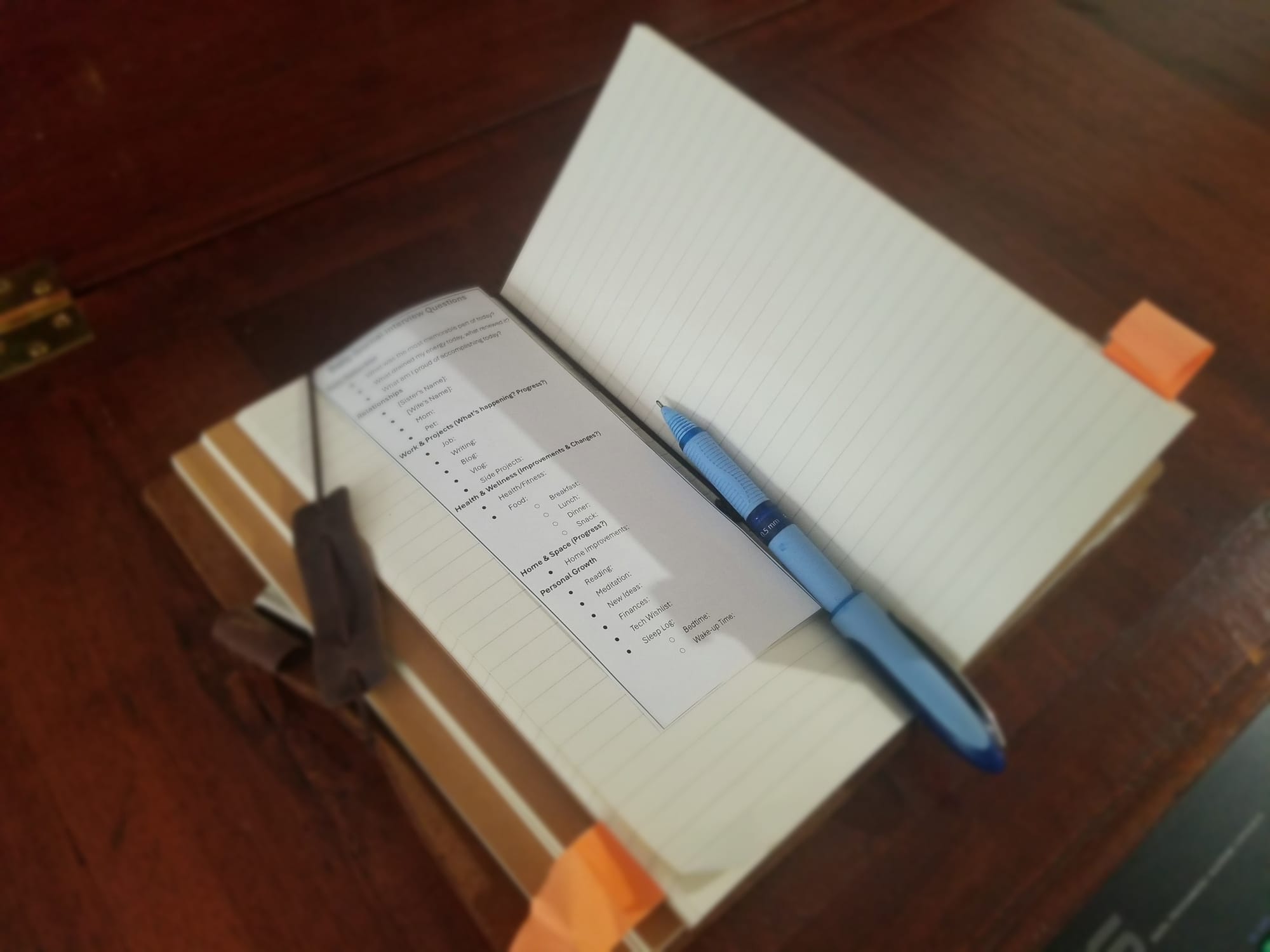 Open lined notebook on a wooden desk with a blue pen and a small printed checklist card tucked inside, with sticky-note tabs on the page.