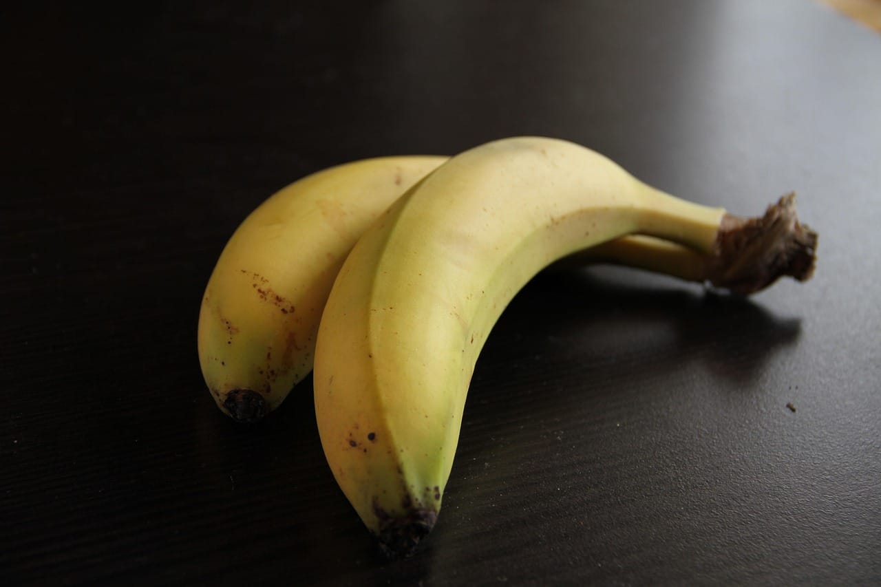 Two ripe bananas on a dark tabletop in soft natural light.