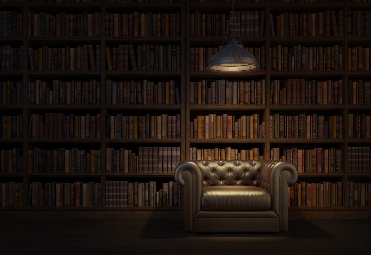 Leather armchair under a hanging lamp in front of tall, dark wooden bookshelves filled with books.